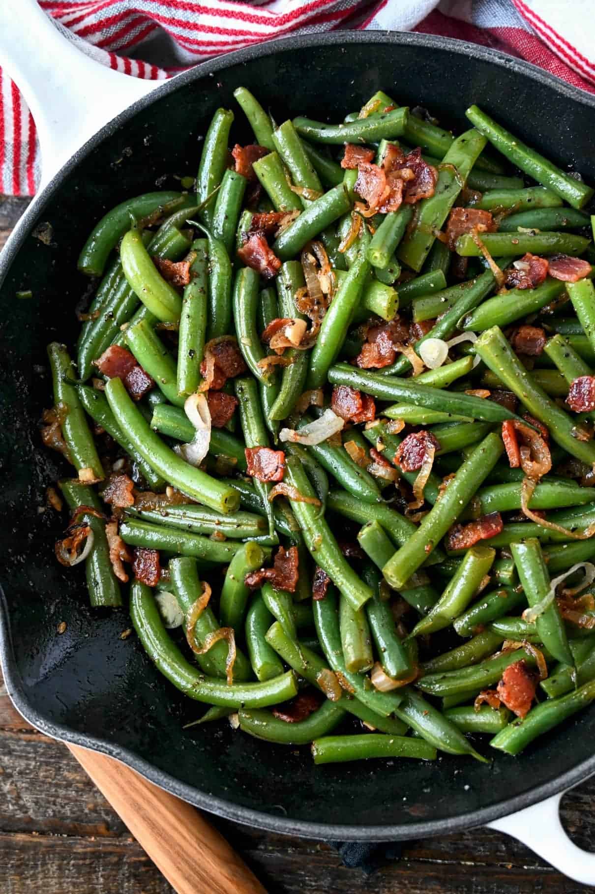 Close up photo of green beans and bacon in a skillet.