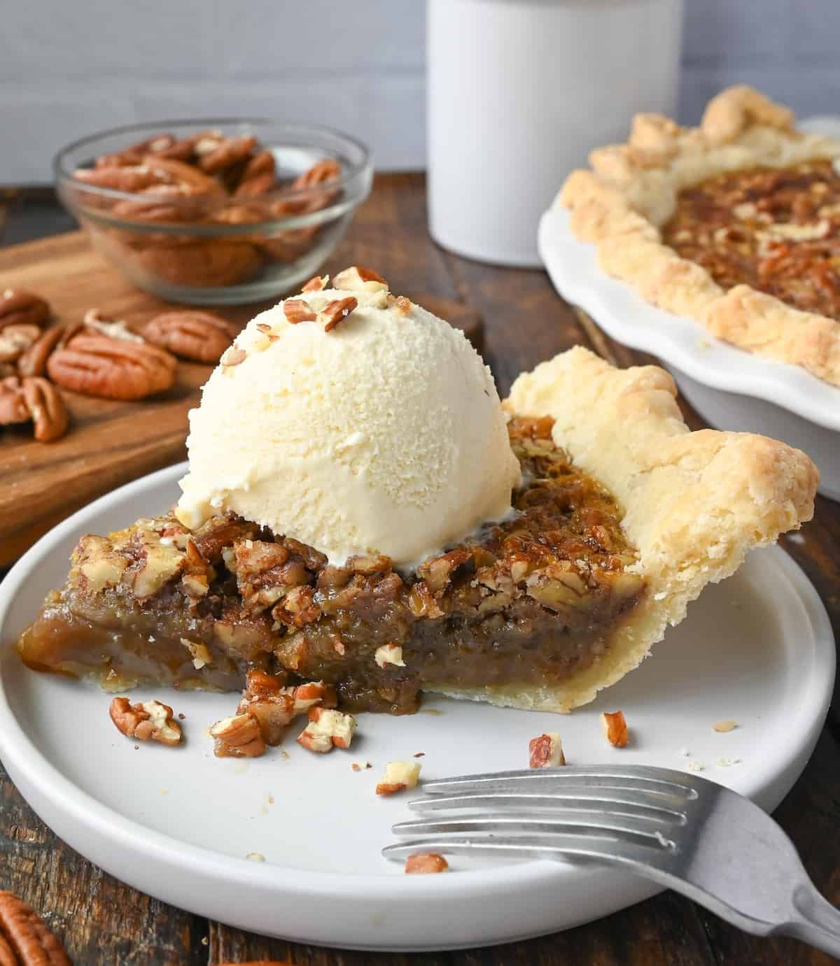 Maple pecan pie on a plate with vanilla ice cream and a fork.