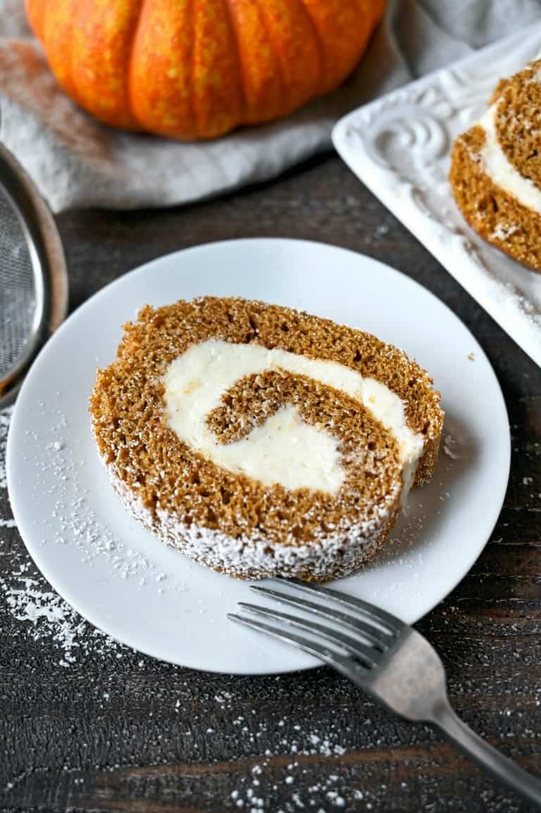 Pumpkin roll cake slice on a small white plate with a fork.