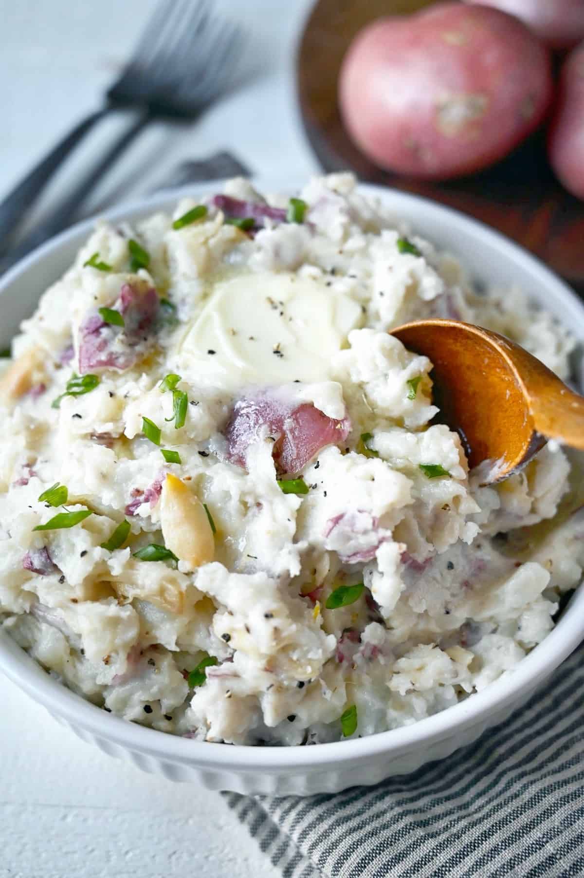 A bowl of mashed red potatoes with a wooden spoon.