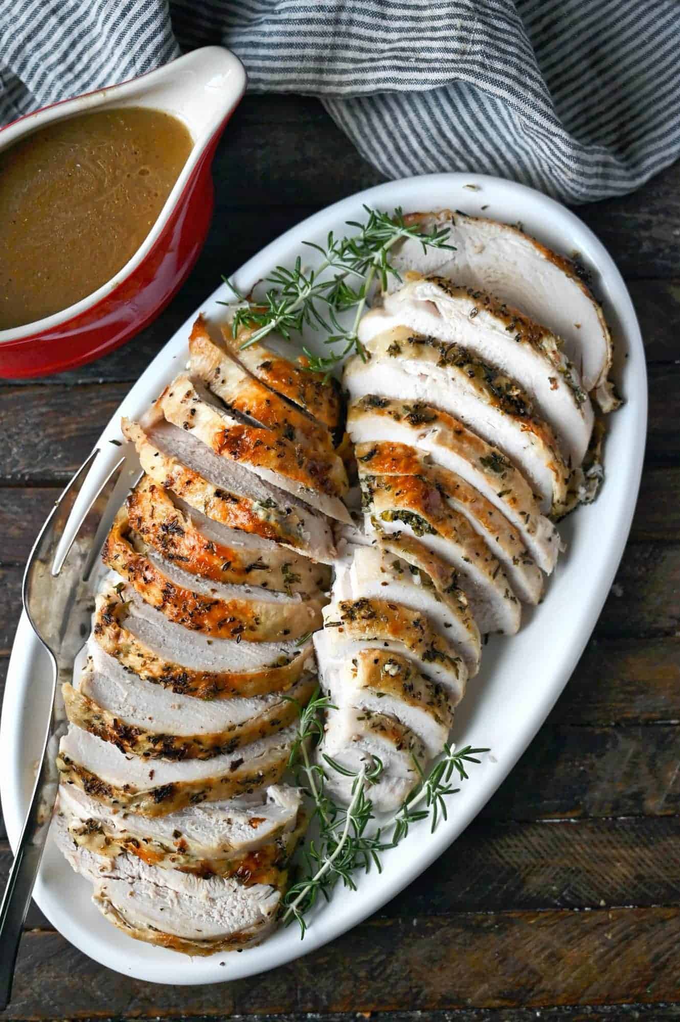 Two turkey breats thinly sliced on a white platter with rosemary sprigs.