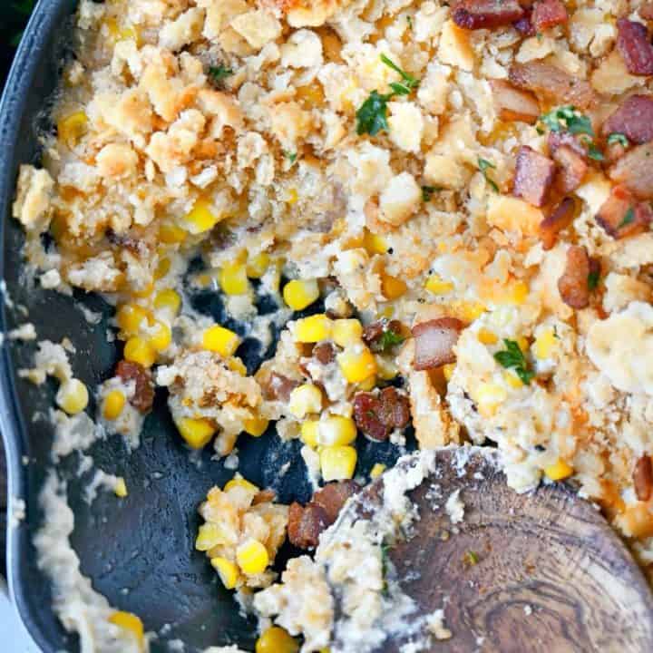 Corn casserole in a skillet with 1/4 miccing and a wooden serving spoon.