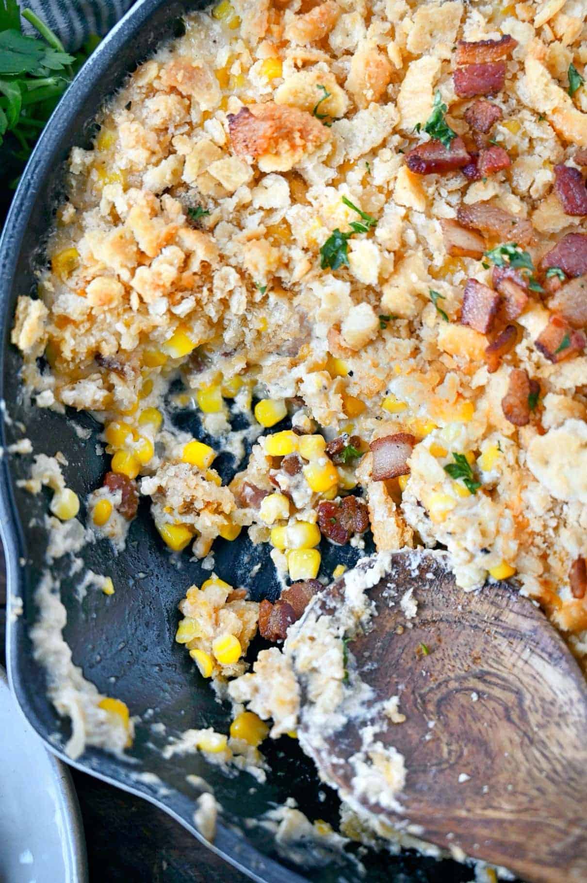 Corn casserole in a skillet with 1/4 miccing and a wooden serving spoon.