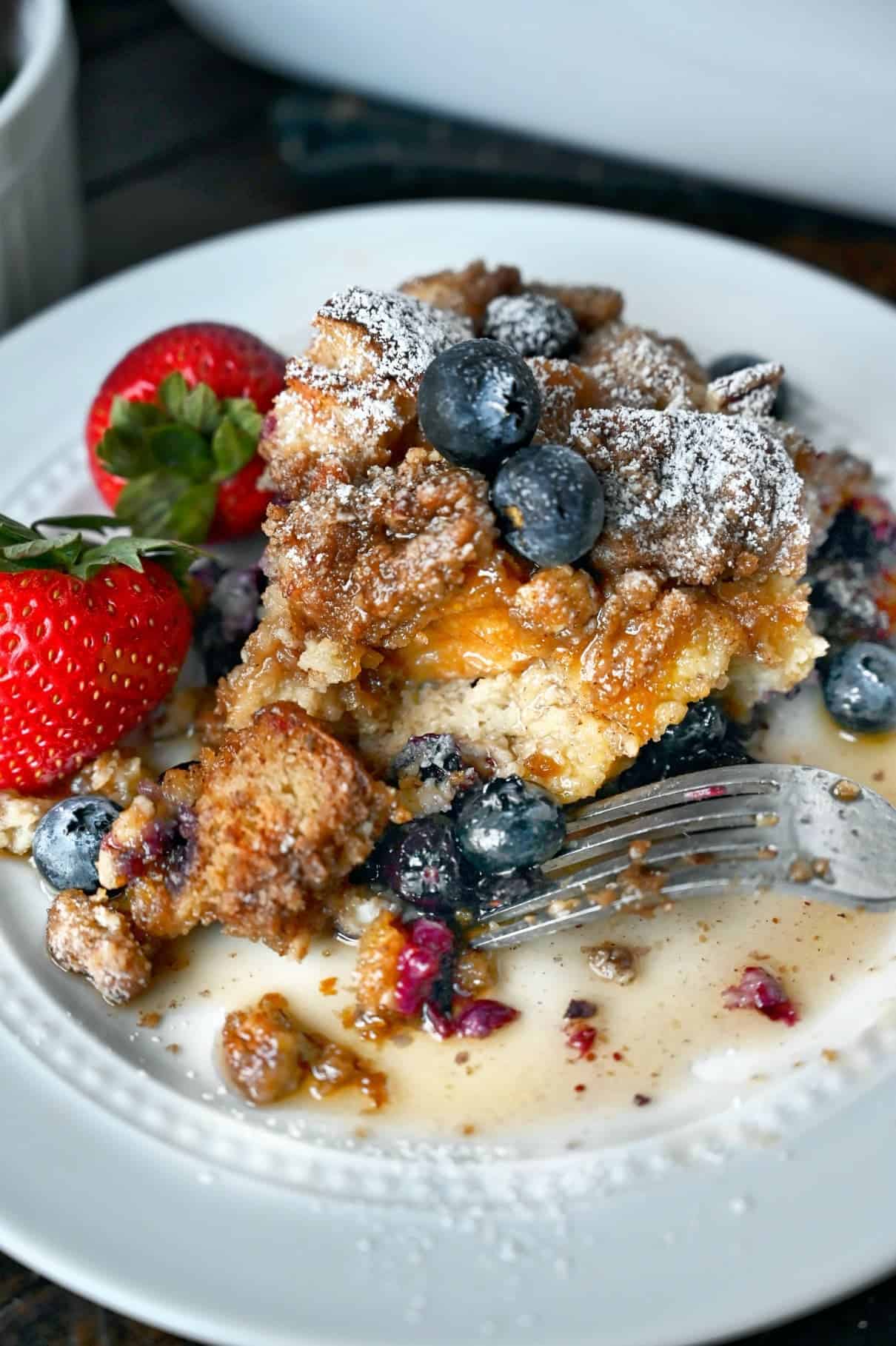 A scoop of blueberry french toast casserole with a fork on a white plate.
