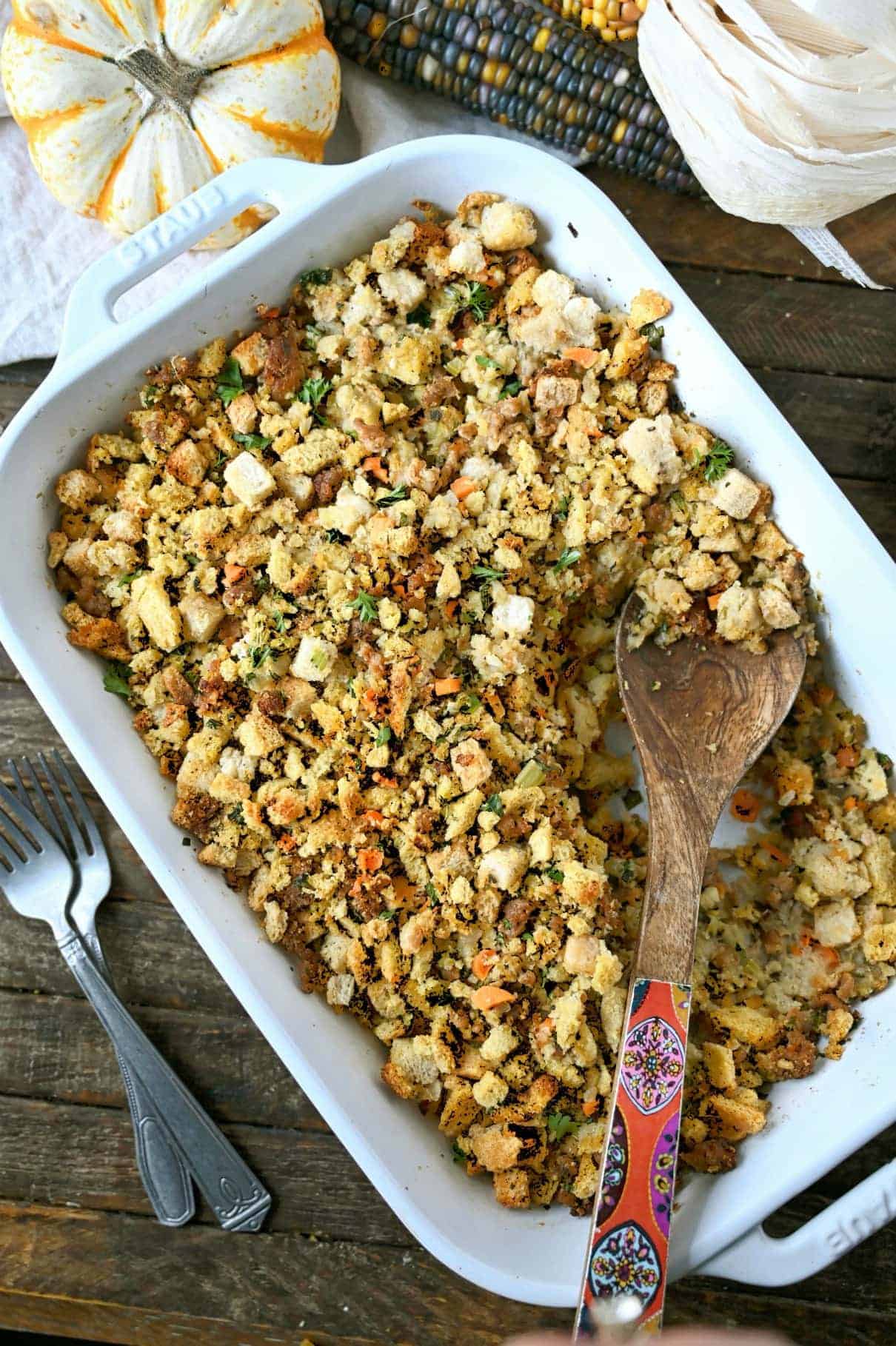 cornbread sausage dressing in a white casserole dish with a wooden serving spoon.