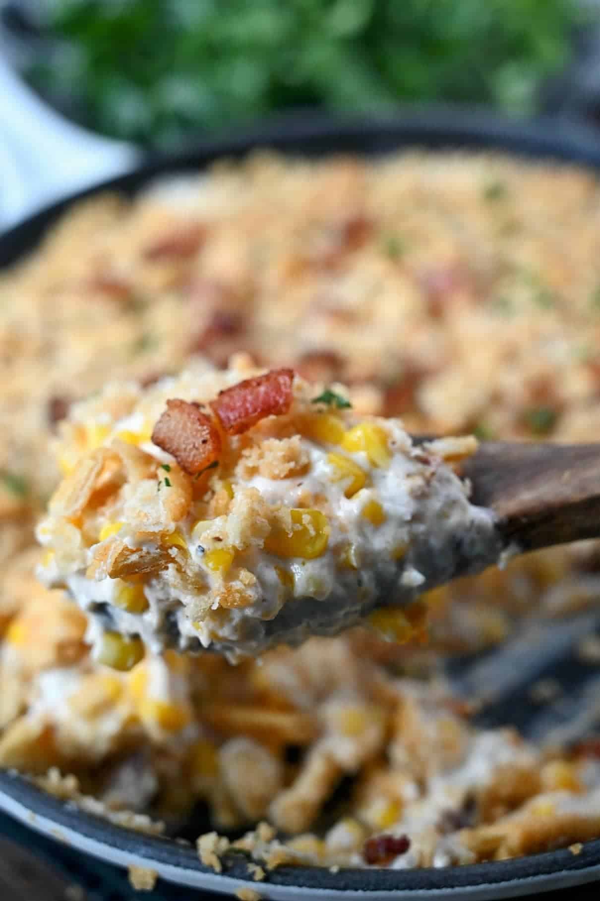 A wooden spoon scooping up some cheesy corn casserole.