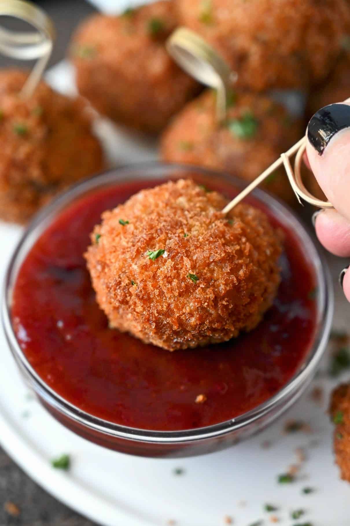 Deep fried breaded ball full of leftover stuffing. On an toothpick and being dipped inot bbq cranberry sauce.