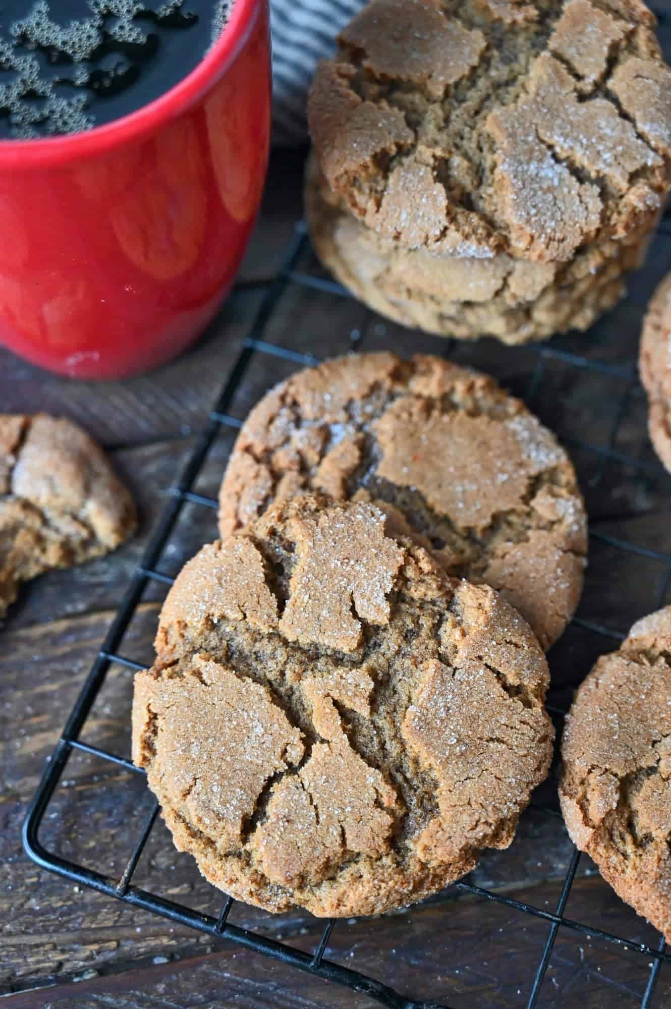 Ginger snap cookies on a cooling rack and a red coffee cup.