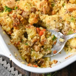 Cornbread dressing in a casserole dish with a spoon taking some out.