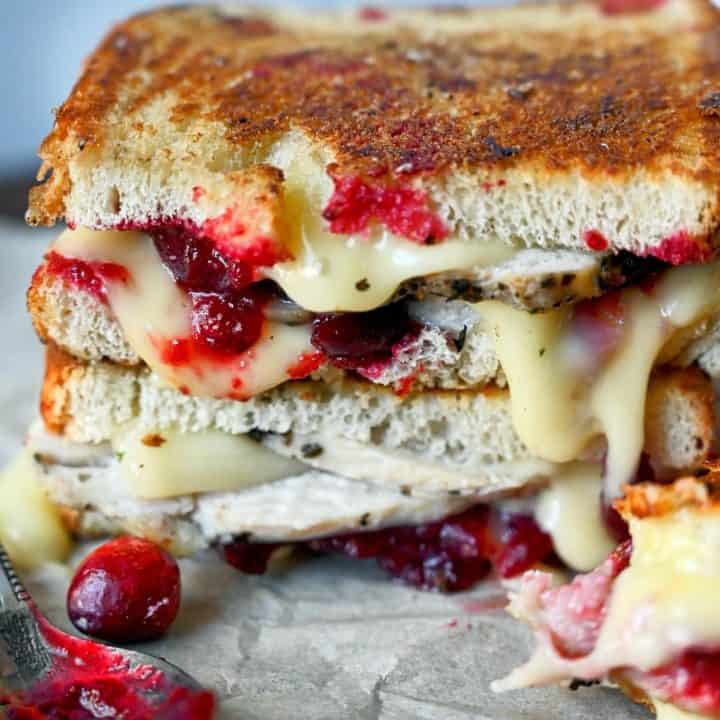 Two turkey cranberry brie sandwich on top of each other with a spoon full of cranberry sauce on the side.