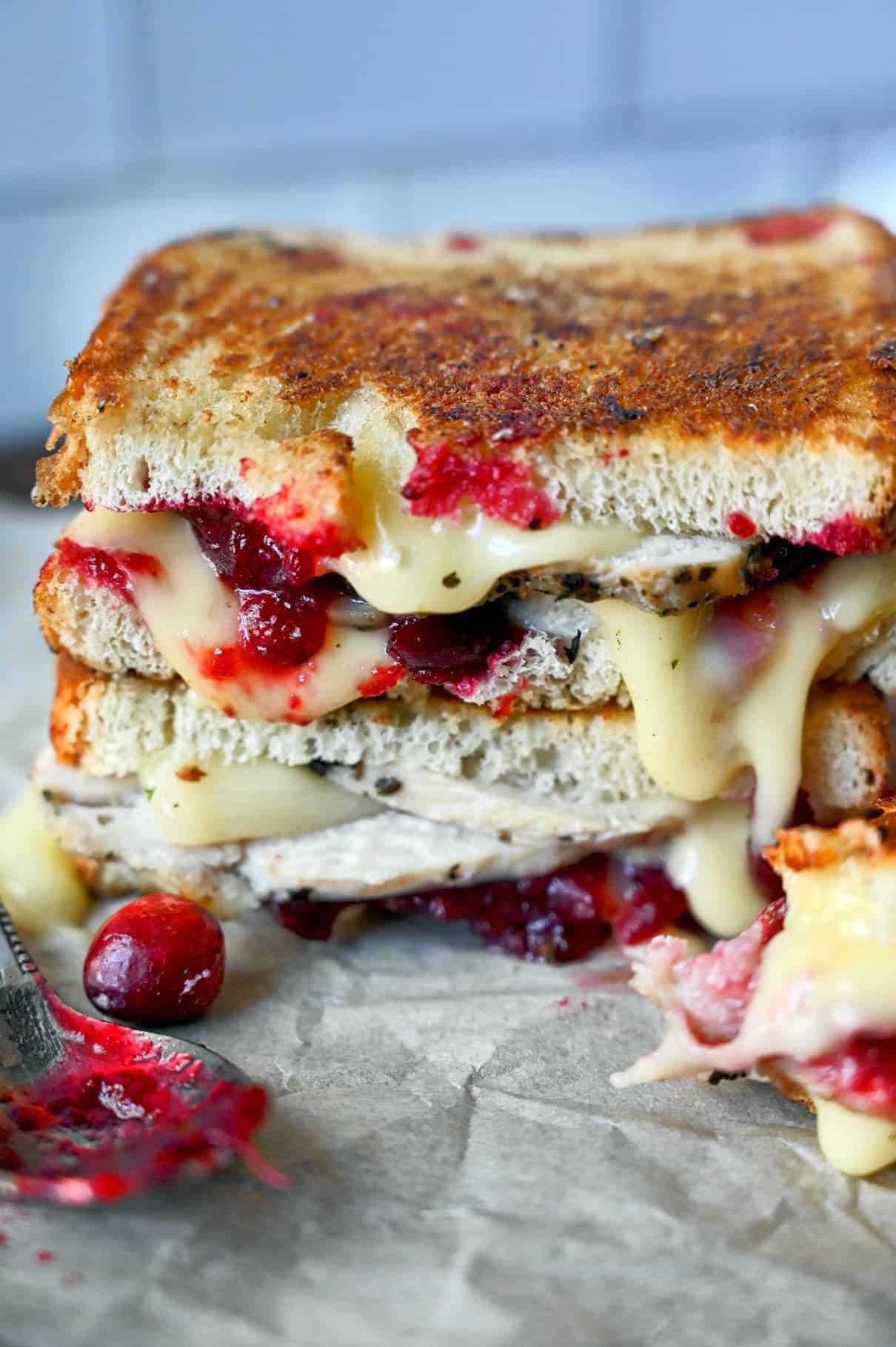 Two turkey cranberry brie sandwich on top of each other with a spoon full of cranberry sauce on the side.