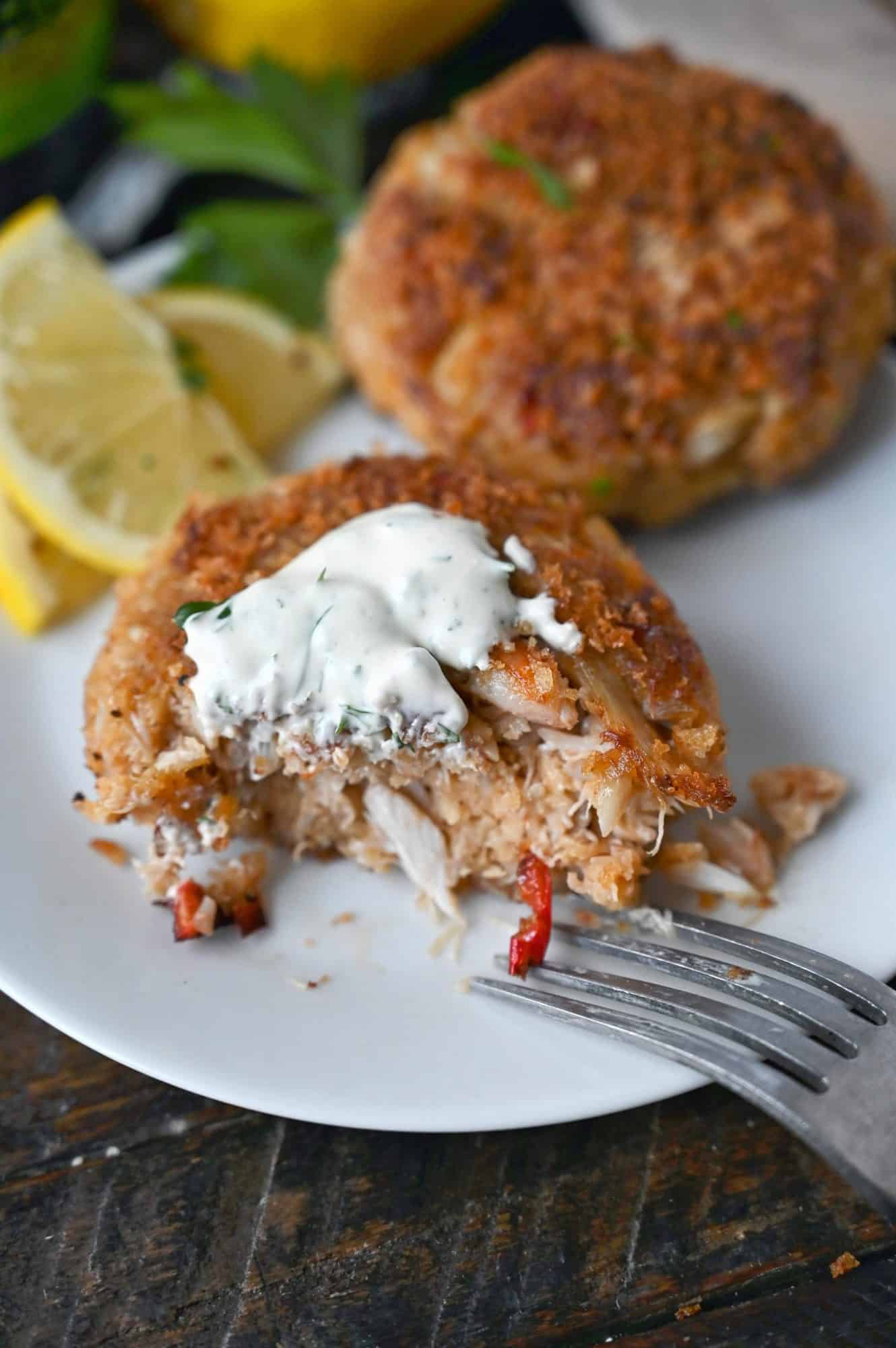 Crab cake wil lemon dill sauce on top and a bite removed and a fork on the side.