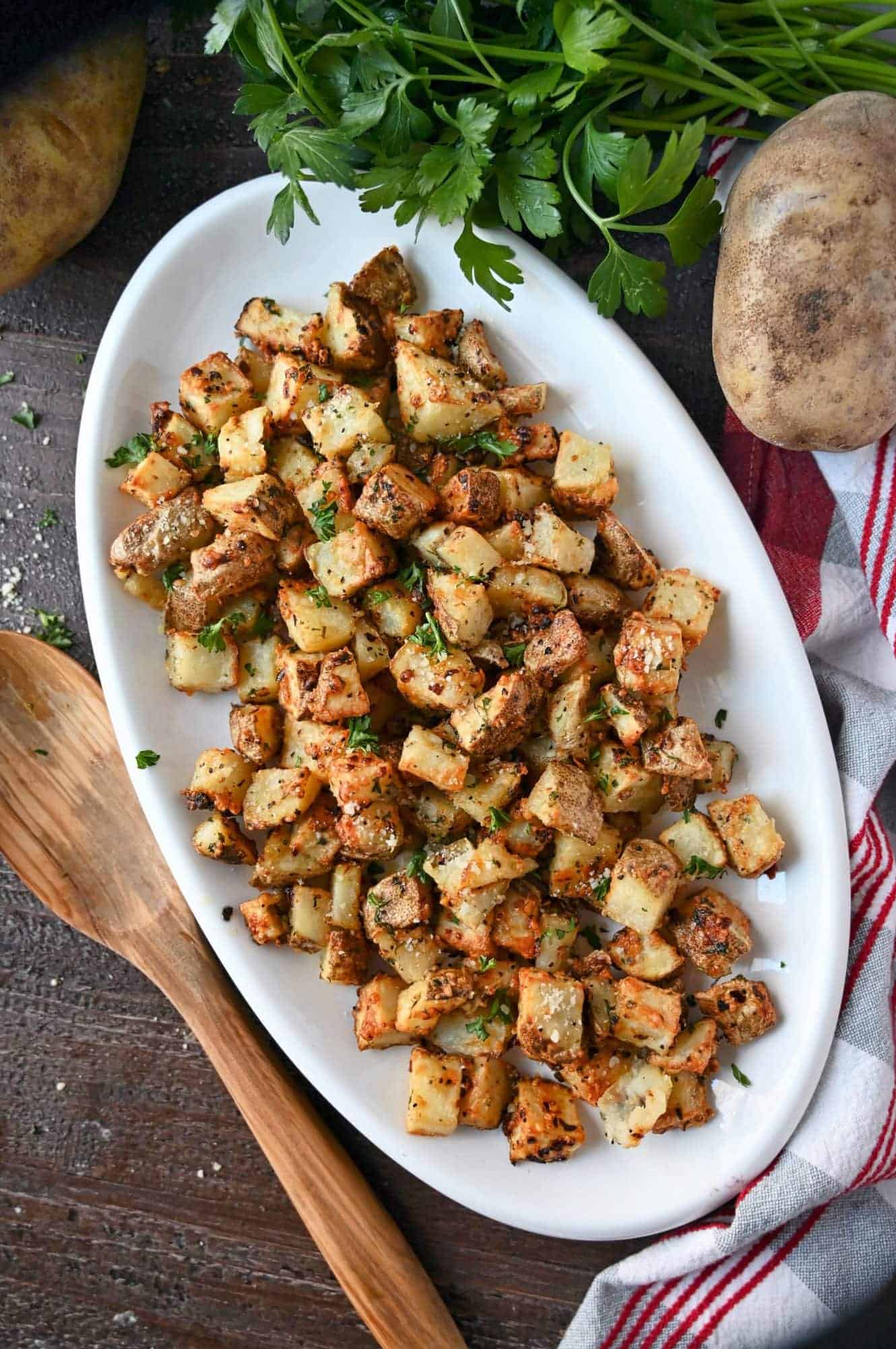 Air fryer garlic parmesan potatoes on a white platter with a wooden spoon on the side.