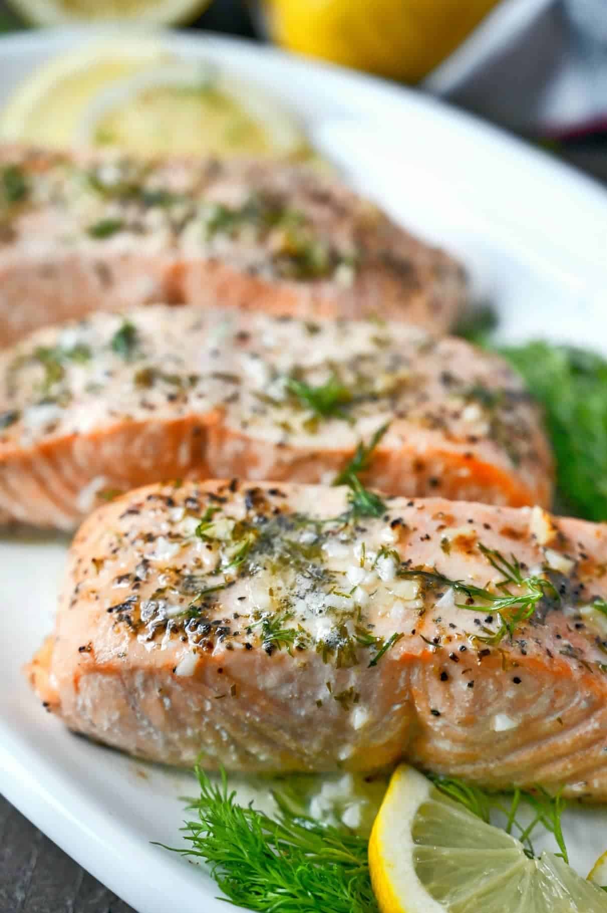 Three salmon filets on a white platter with lemon butter sauce on top.