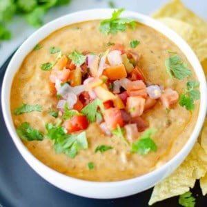 A bowl of queso with pico de gallo on top.