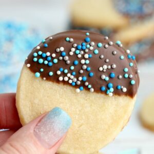 Chocolate dipped butter cookie with blue sprinkles being held in hand.