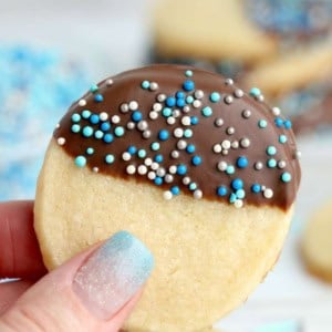 Chocolate dipped butter cookie with blue sprinkles being held in hand.