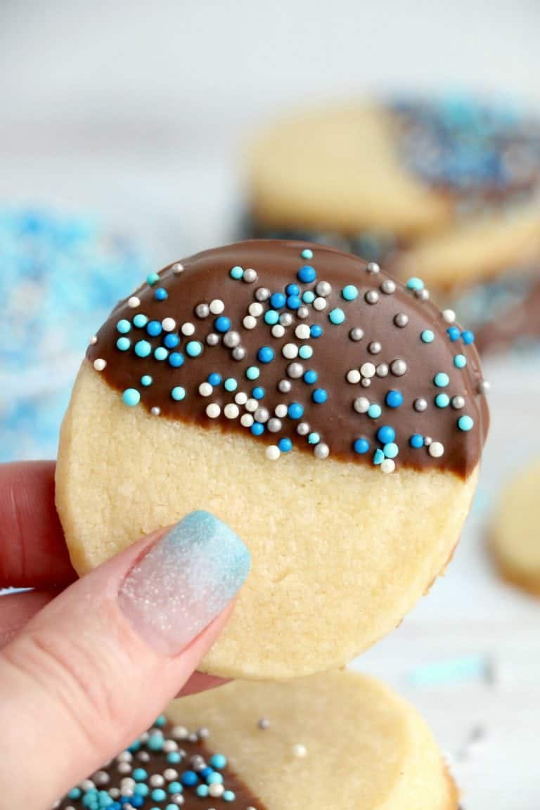 Chocolate dipped butter cookie with blue sprinkles being held in hand.