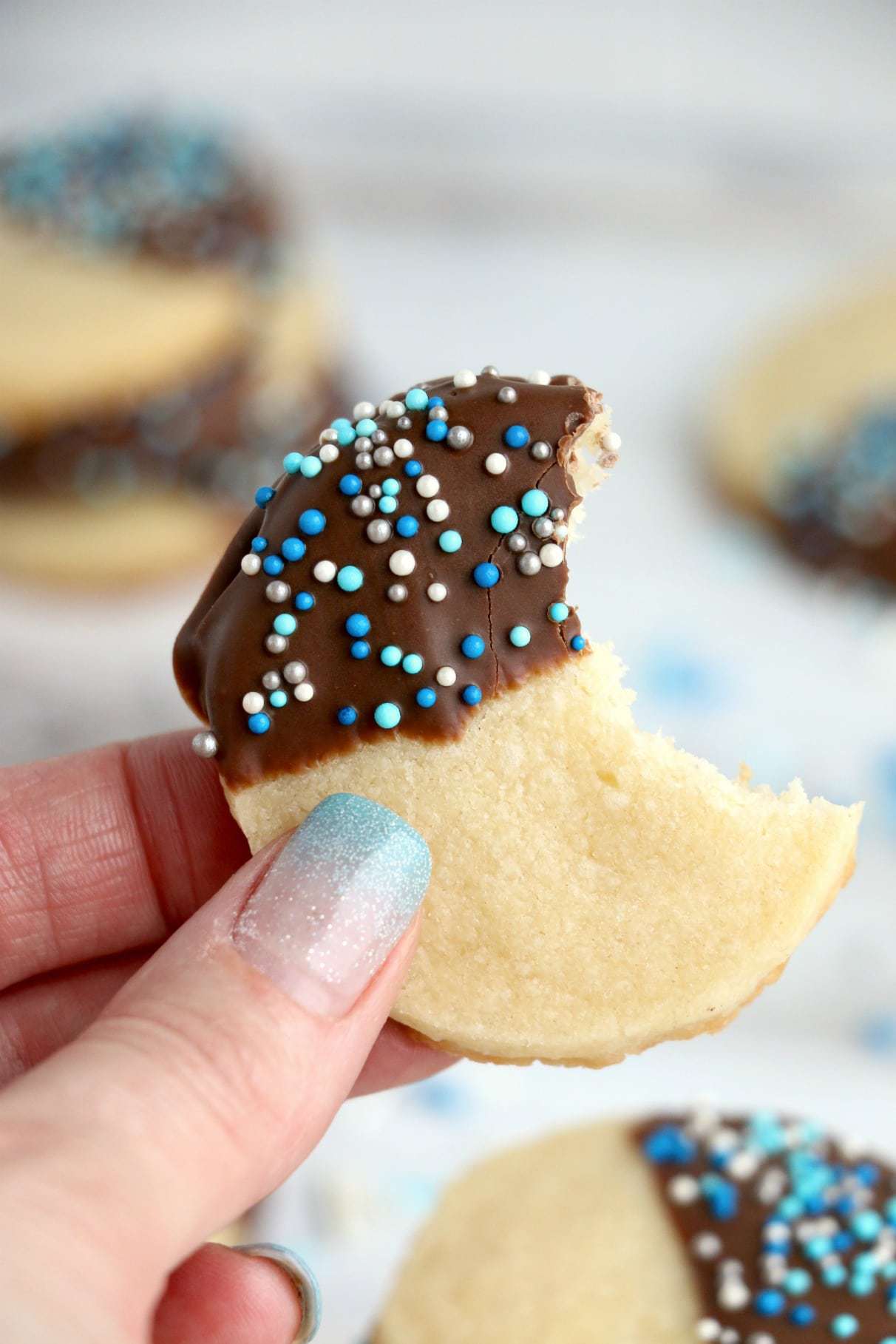 Chocolate dipped cookie with a bite being held in a hand.