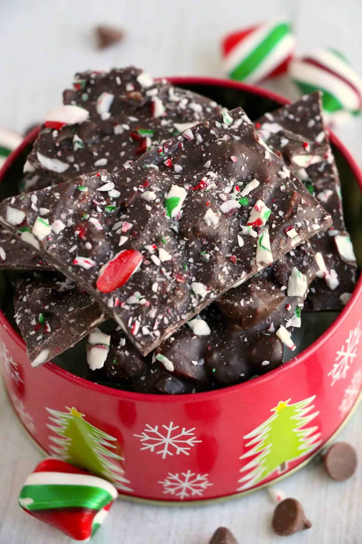 Chocolate peppermint bark piled into a christmas tin with mint candies on the side.