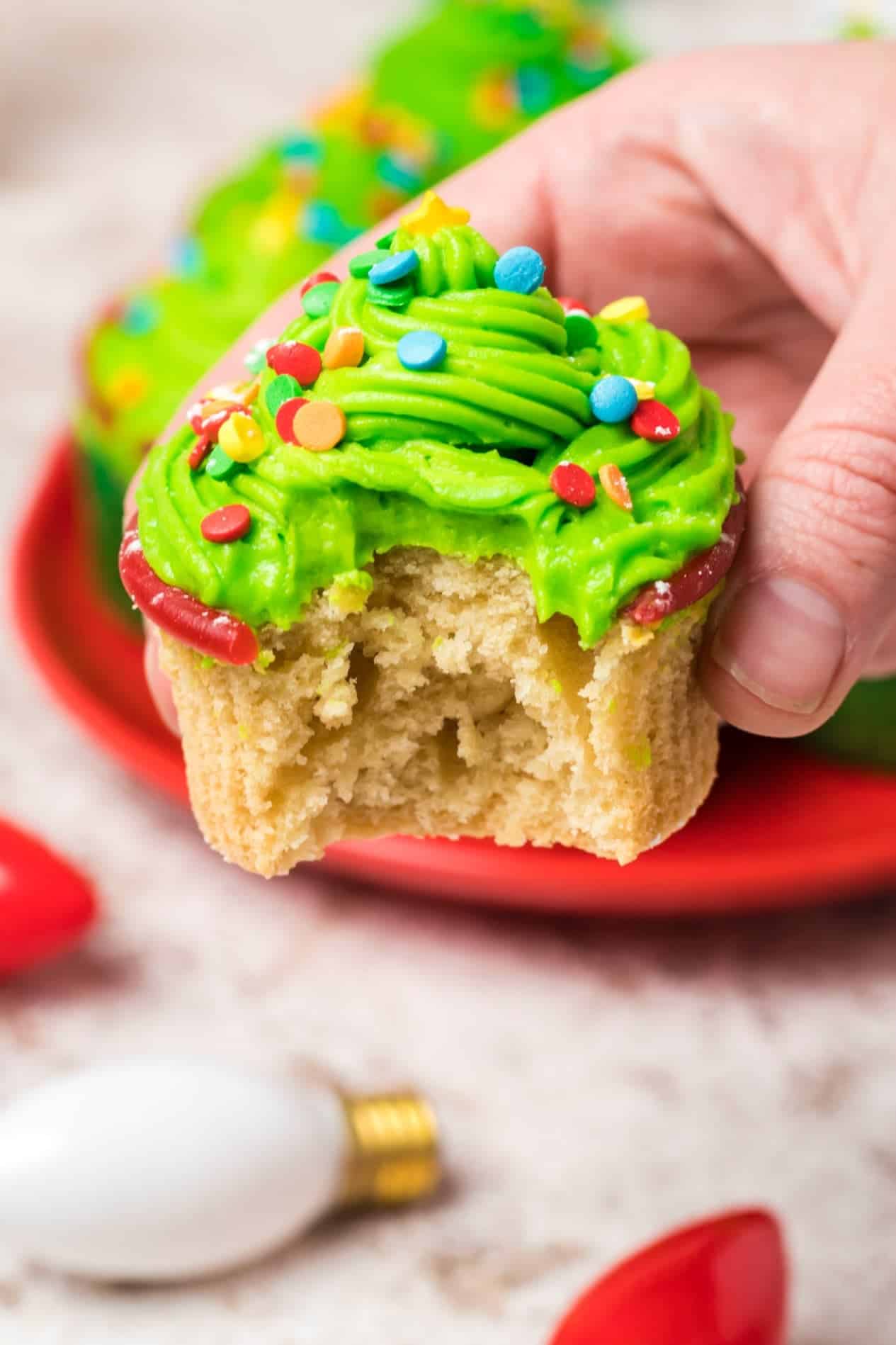 A Christmas tree cupcake being held in a hand with a bite out of it.