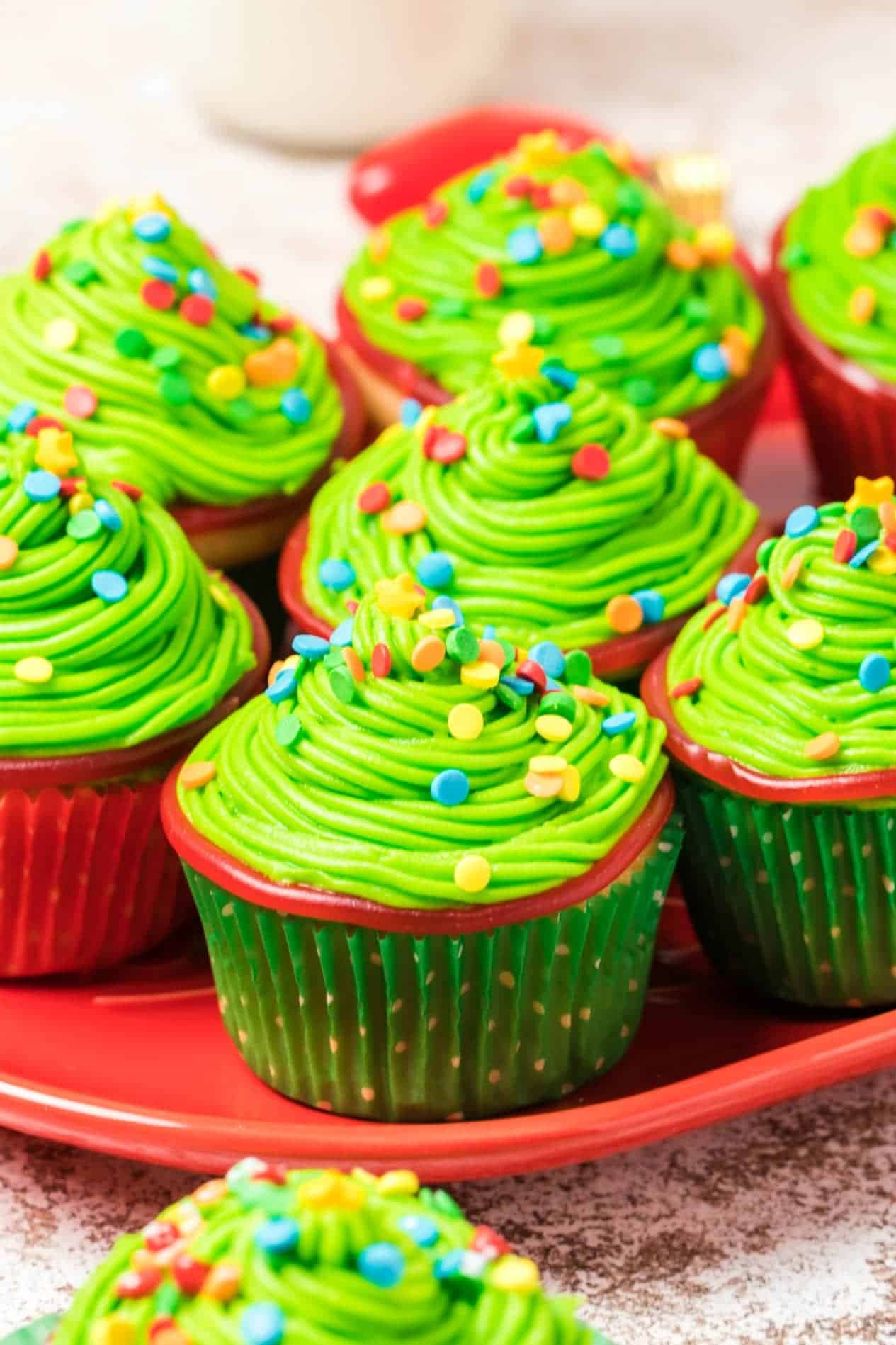 Seven Christmas tree cupcakes on a red platter.