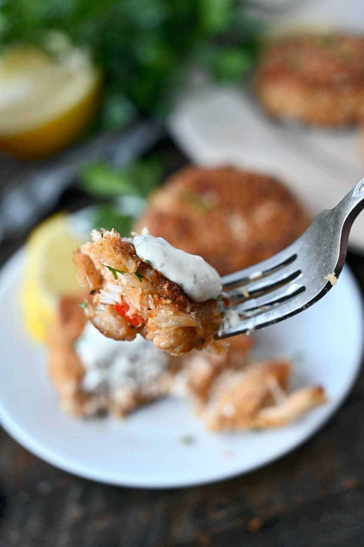 A bite of crab cake and a dollop of lemon dill sauce on a fork.