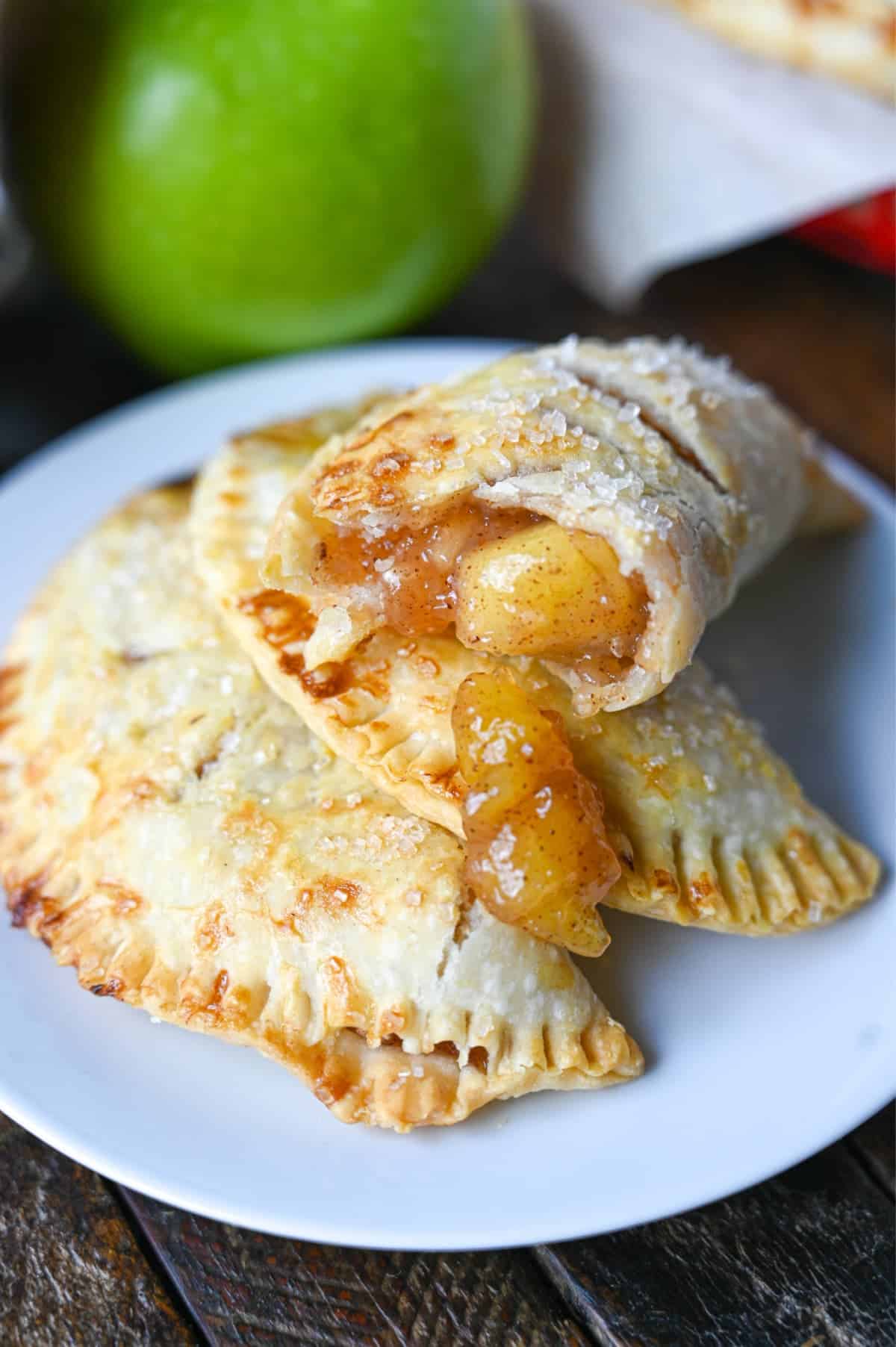 Apple hand pie with a bit out of it piled on top of two other hand pies on a white plate.