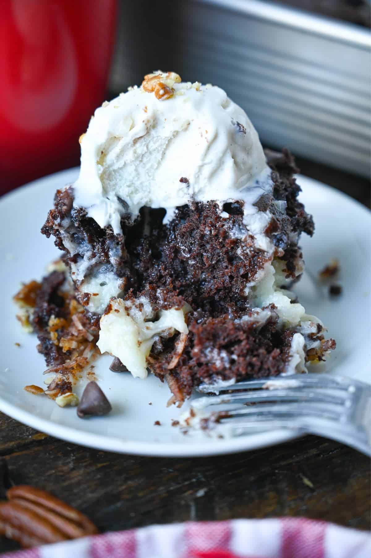 A piece of chocolate earthquake cake on a white plate with vanilla ice cream on top and a bite out of it.