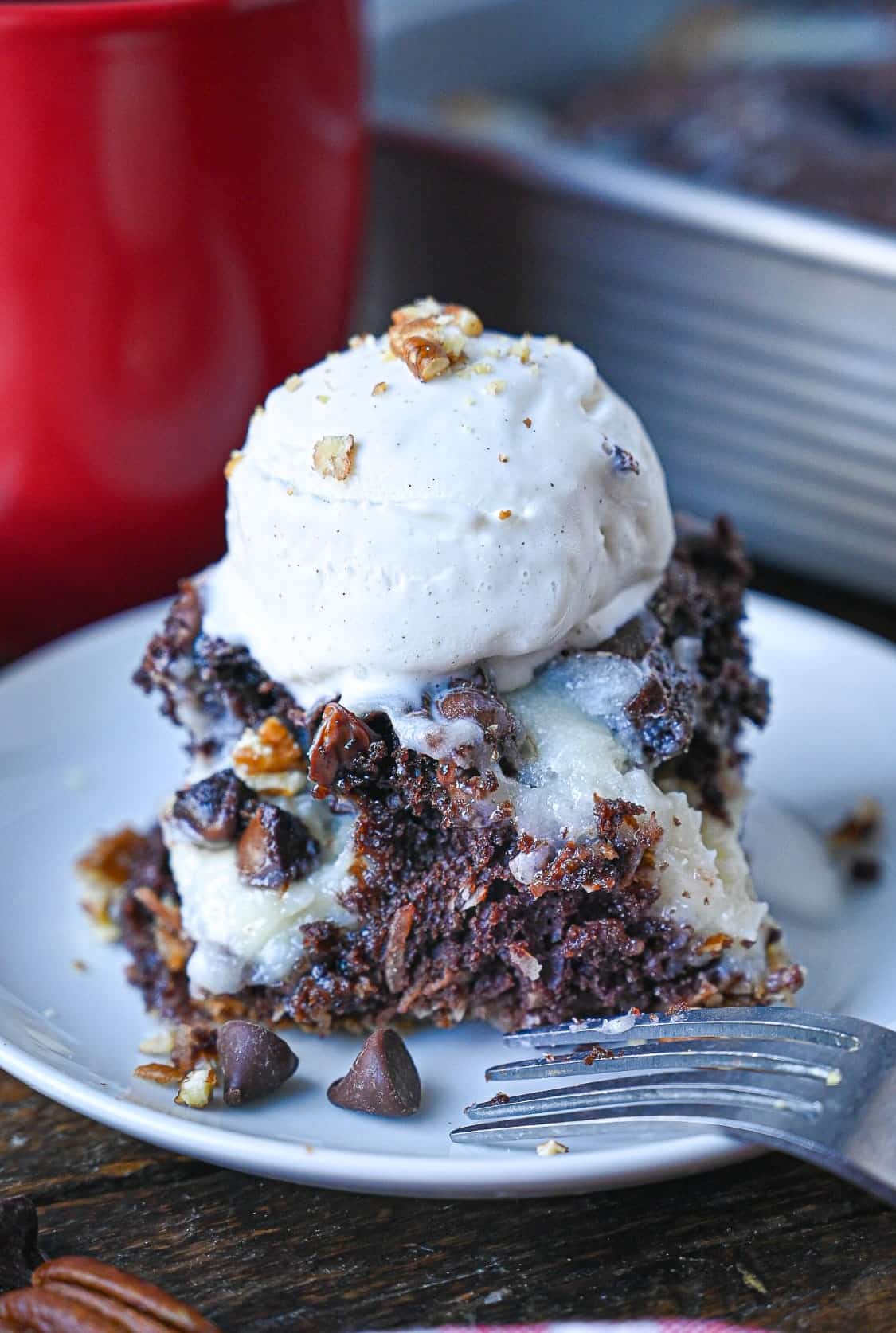 A piece of chocolate earthquake cake on a white plate with a scoop of vanilla ice cream on top.