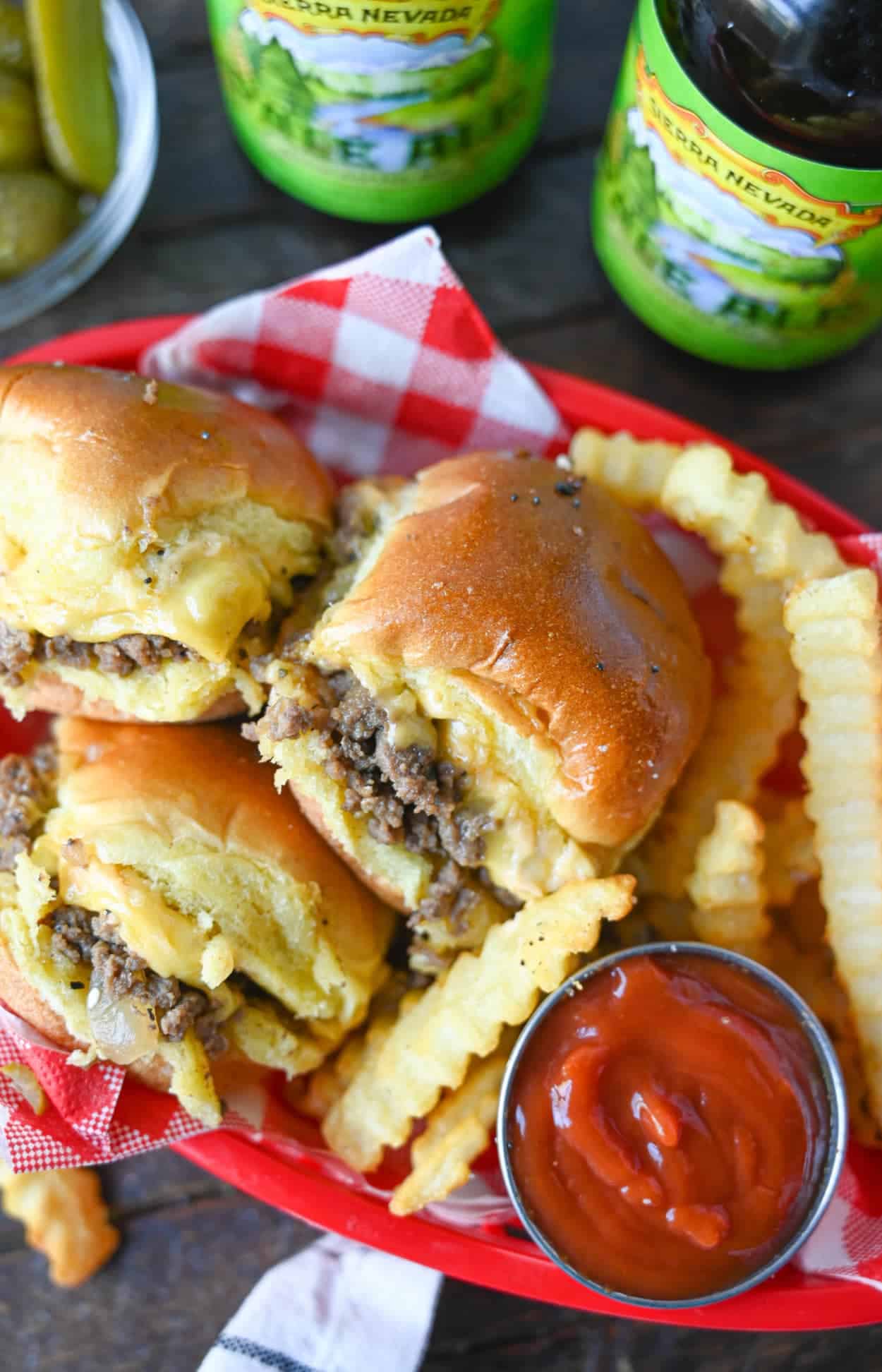 Three chopped cheeseburger sliders in a red serving basket with fries and ketchup.