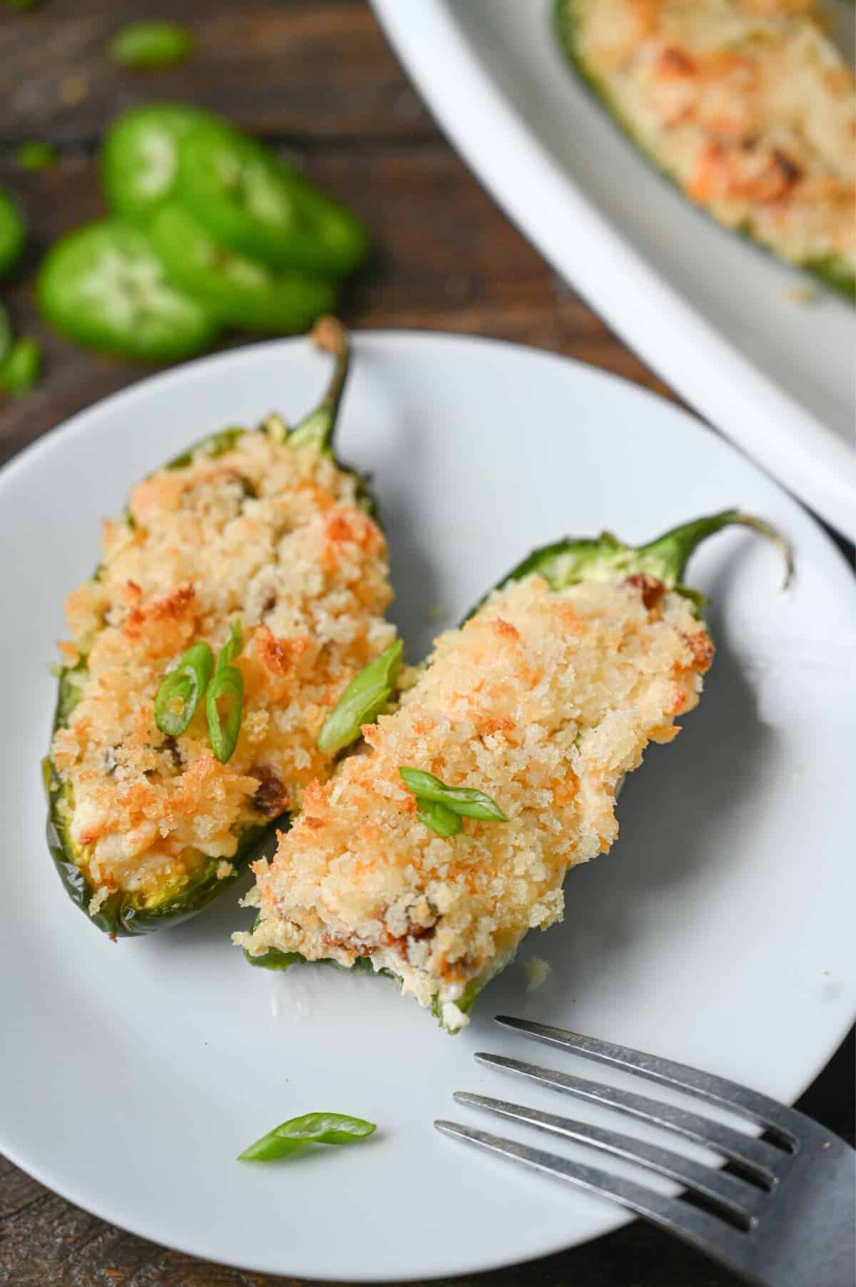 Two jalapenos on a small white plate with a bite out of one.