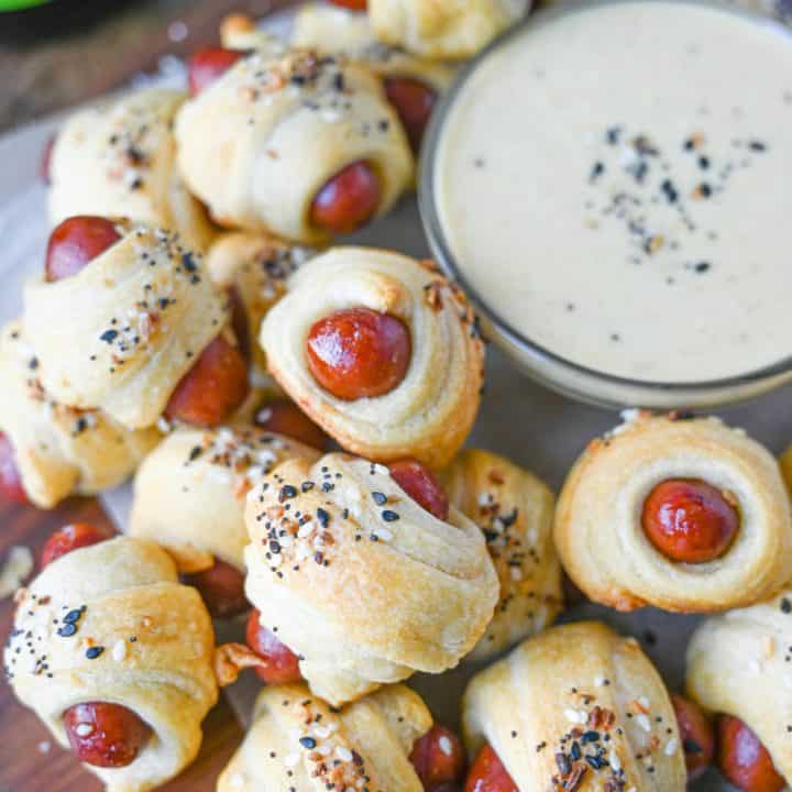 Pigs in a blanket piled on tope of each other with a side of honey mustard in a small dish.