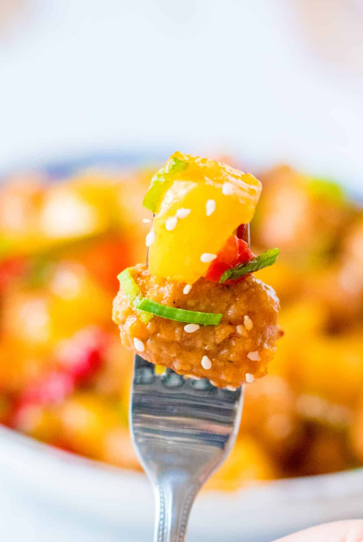 Sweet and sour meatball with pineapple and a red pepper on a fork.