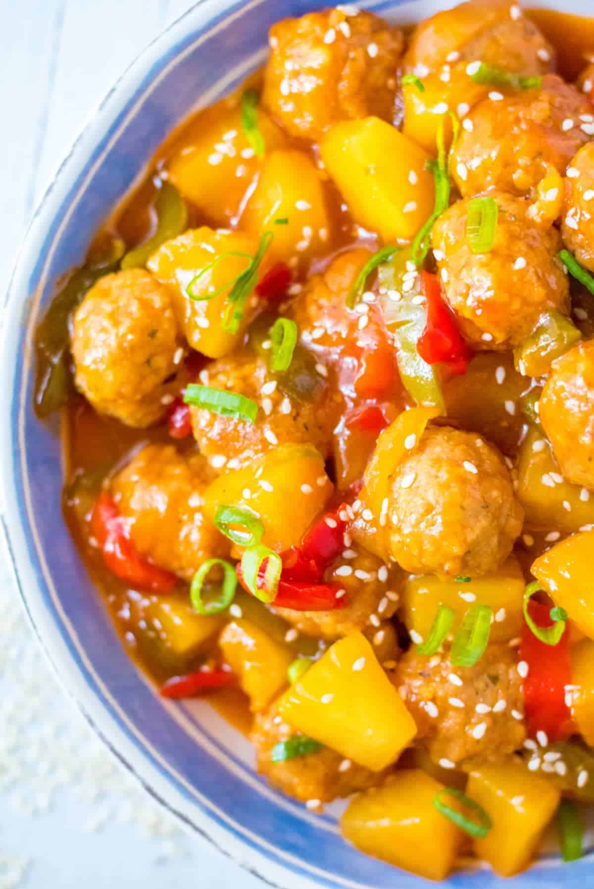 Sweet and sour meatballs in a bowl with pinapple and red peppers. Sesame seeds sprinkled on top.