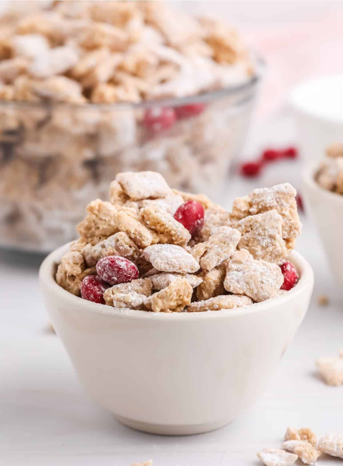A side photo of Valentines muddy buddies in a small white bowl, with a large bowl in the background.