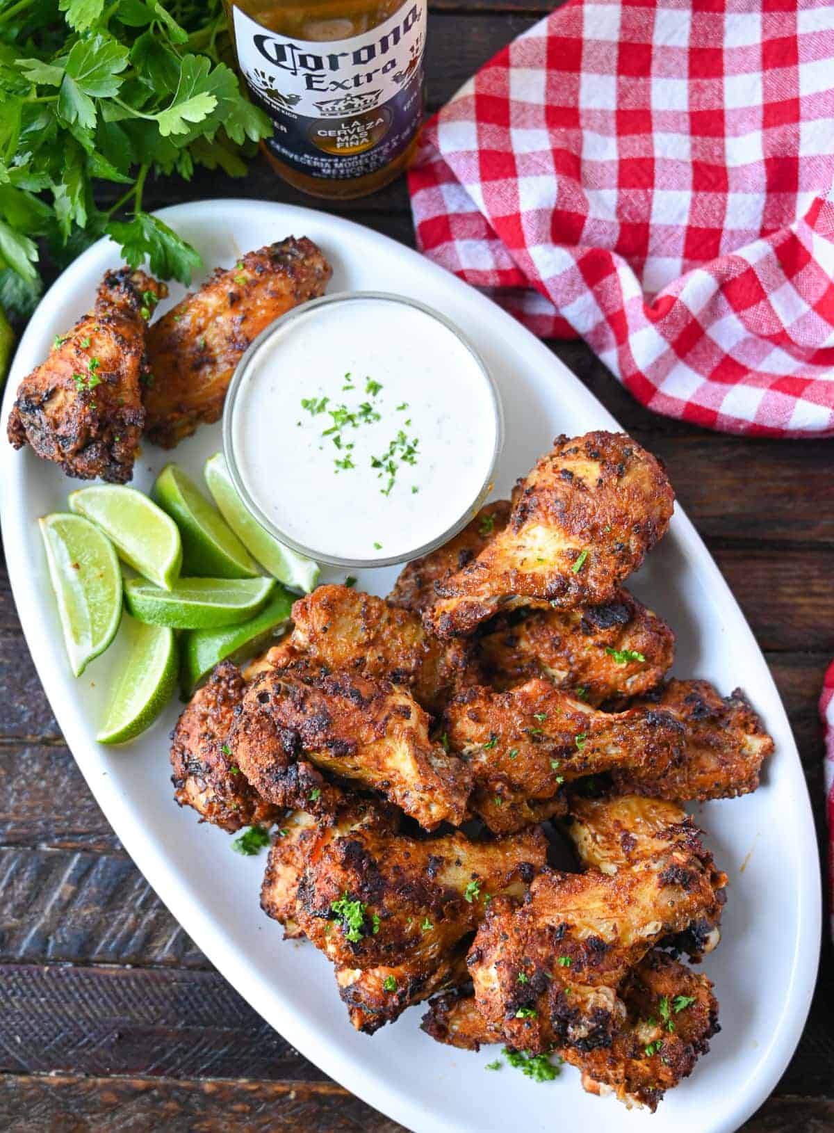 Air fryer old bay chicken wings on an oval white plate with a side of ranch dressing and lime slices.