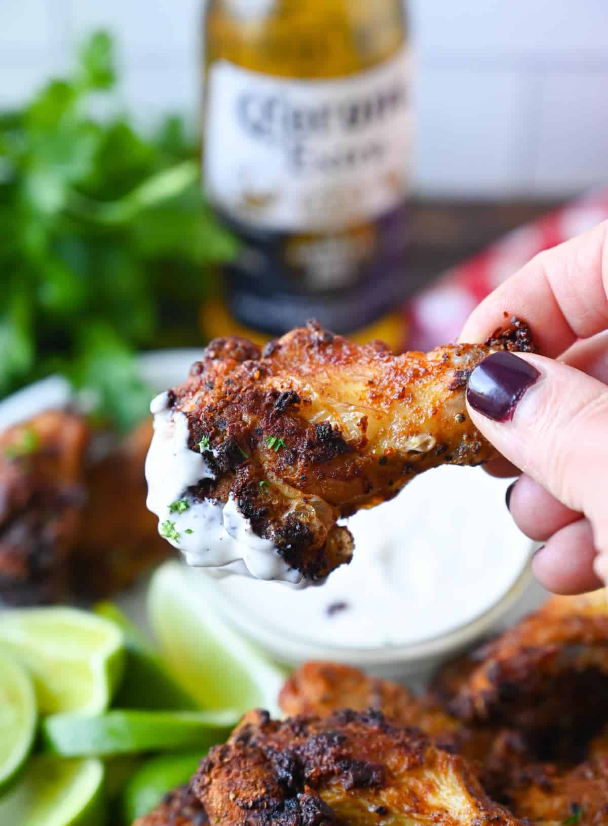 A chicken wing being picked up and that has been dipped in ranch dressing.