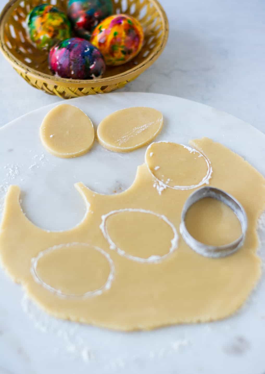 Sugar cookie dough that has been rolled out and a egg shaped cookie cutter.