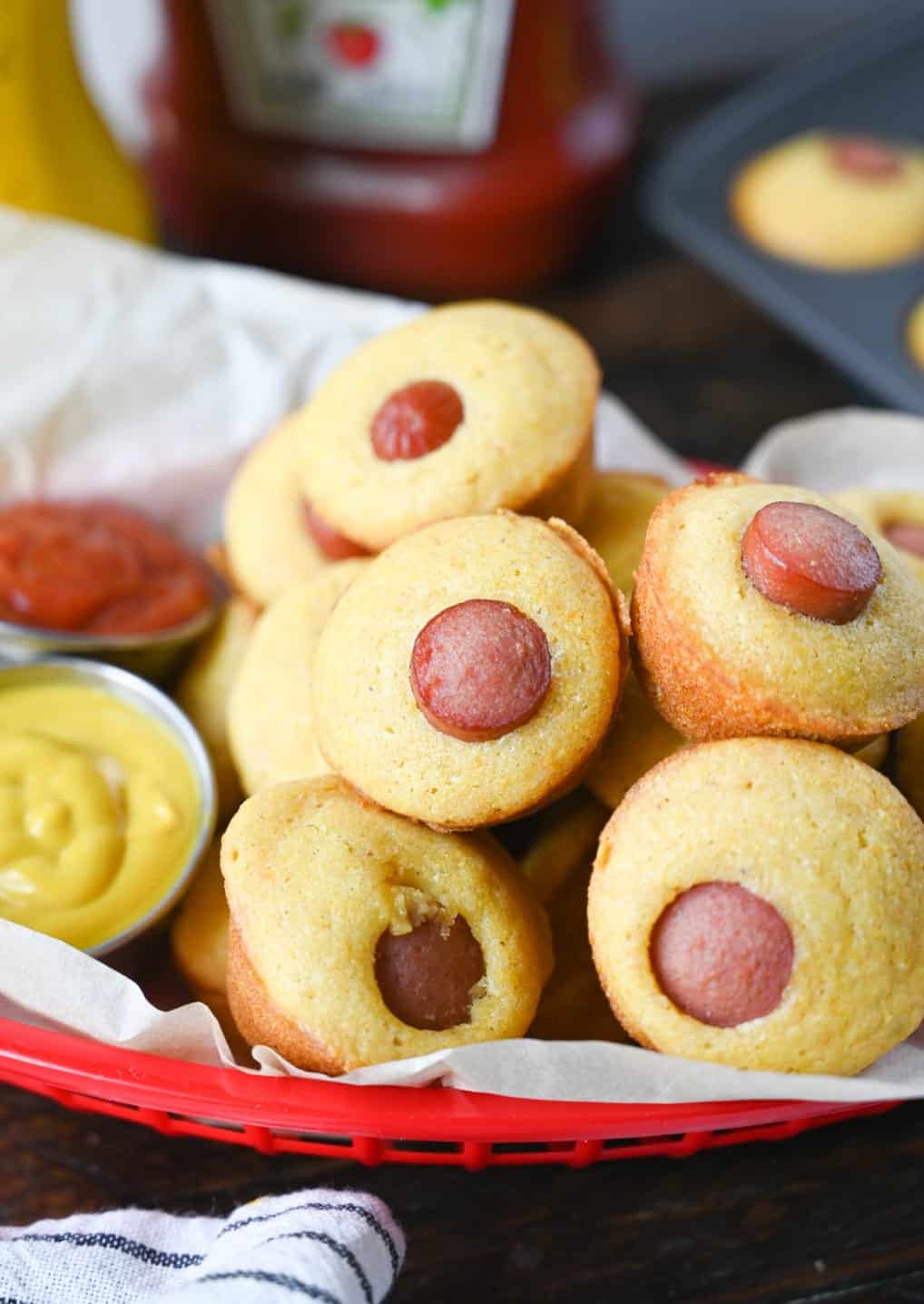 Mini corn dog muffins in a red basket with a side of ketchup and mustard.