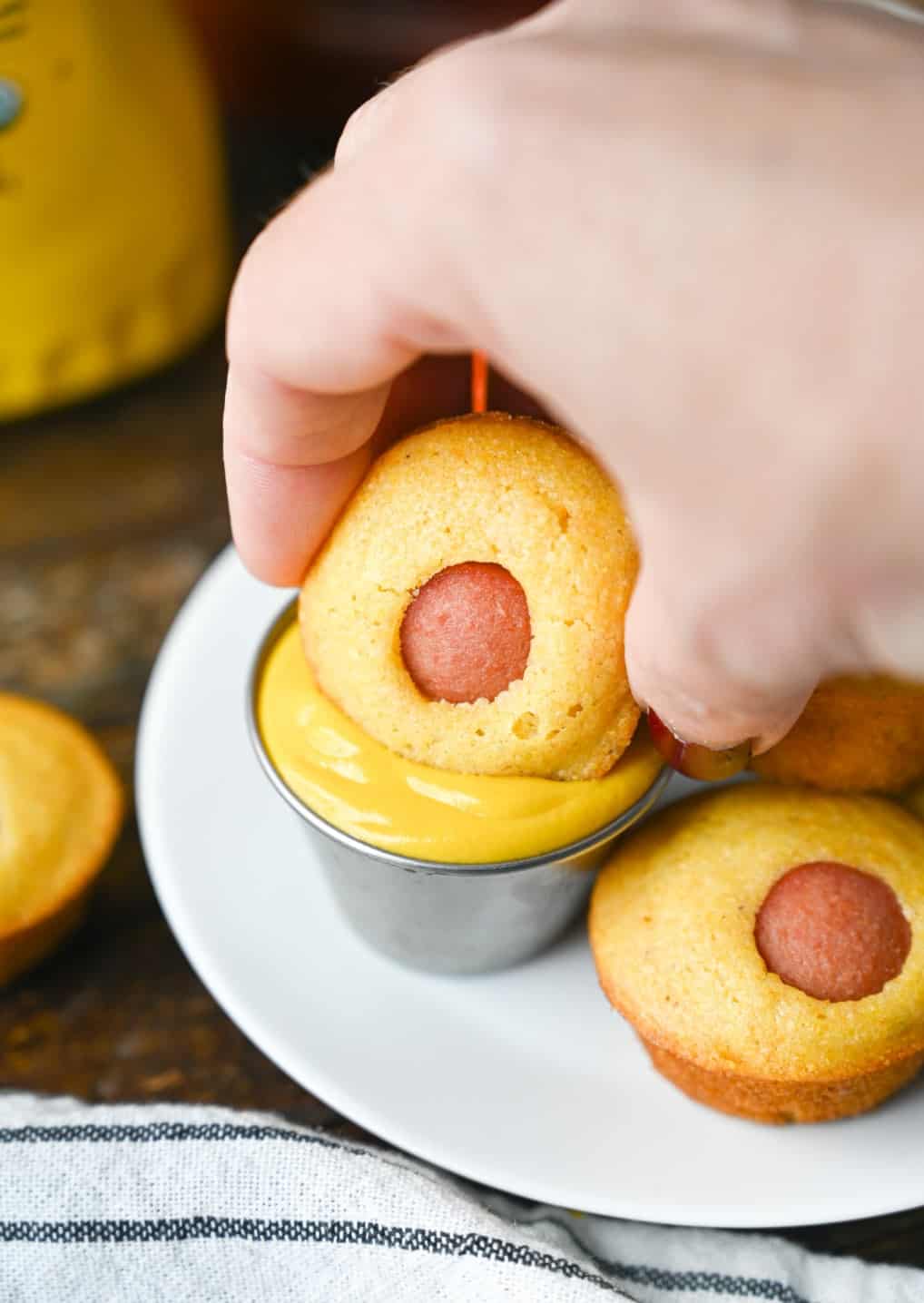 One mini corn dog muffin being dipped into mustard.