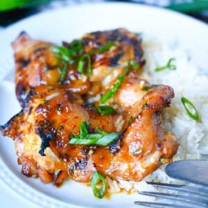 Peach chipotle chicken placed on top of coconut rice on a white plate.