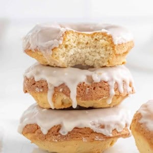 Three baked glazed donuts stacked on top of each other with a bite out of the top one.