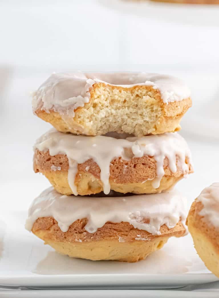 Three baked glazed donuts stacked on top of each other with a bite out of the top one.