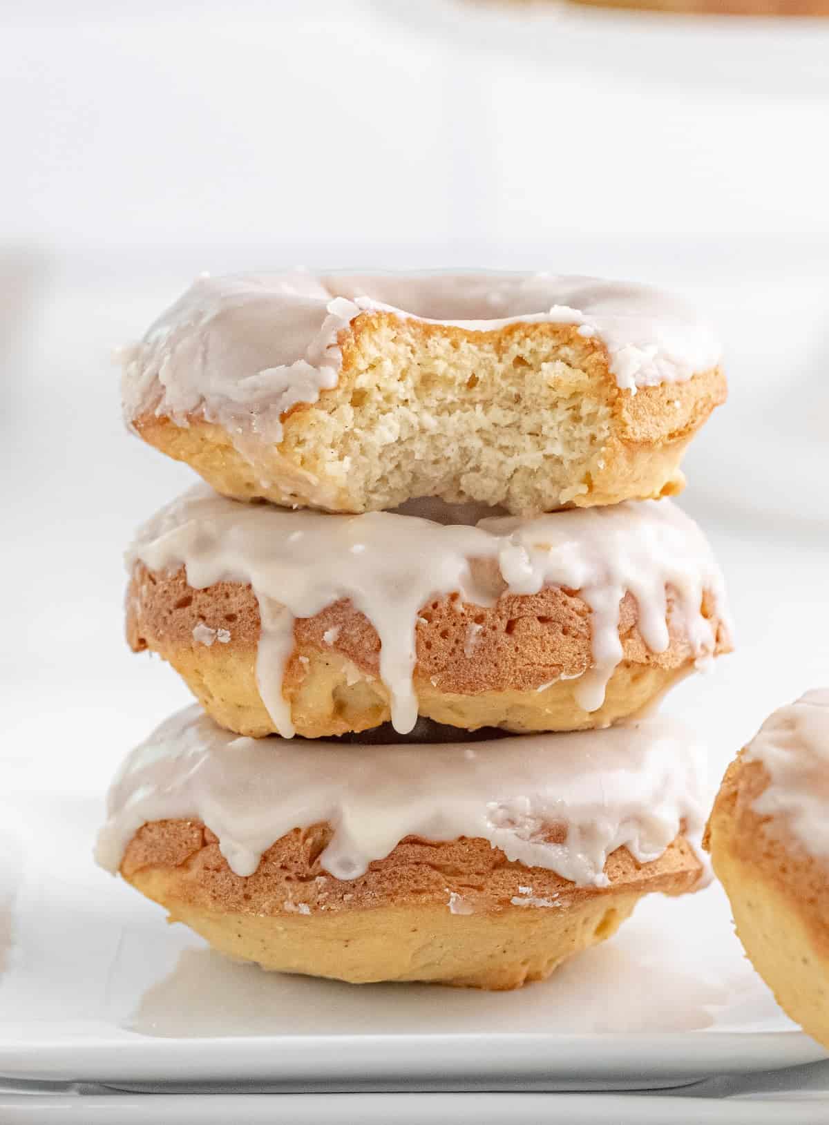 Three baked glazed donuts stacked on top of each other with a bite out of the top one. 