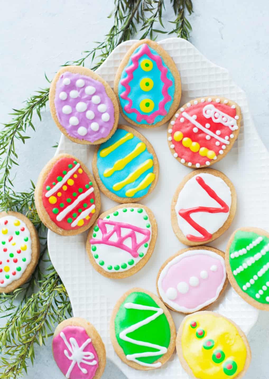 Several decorated Easter egg cookies laying on a white platter.