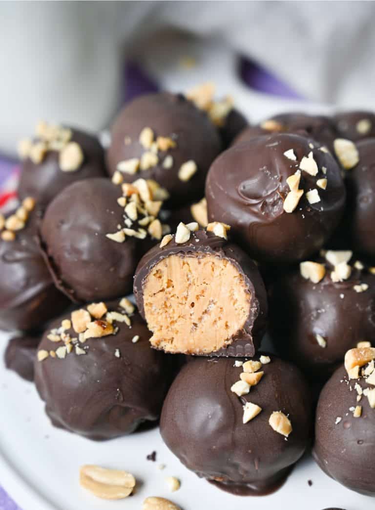 A pile of peanut butter balls on a whilte plate with one that had a bite out of it.