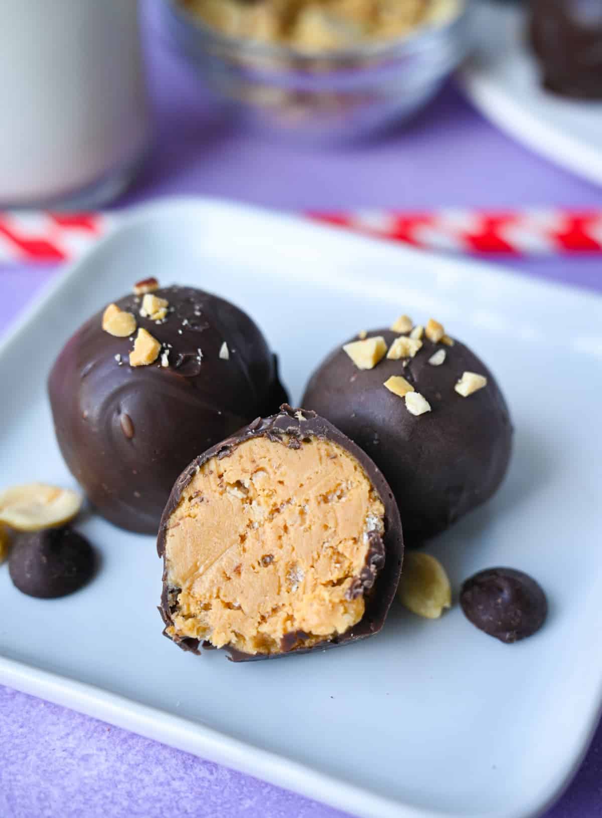 Three peanut butter balls on a small square white plate with a bite out of one.