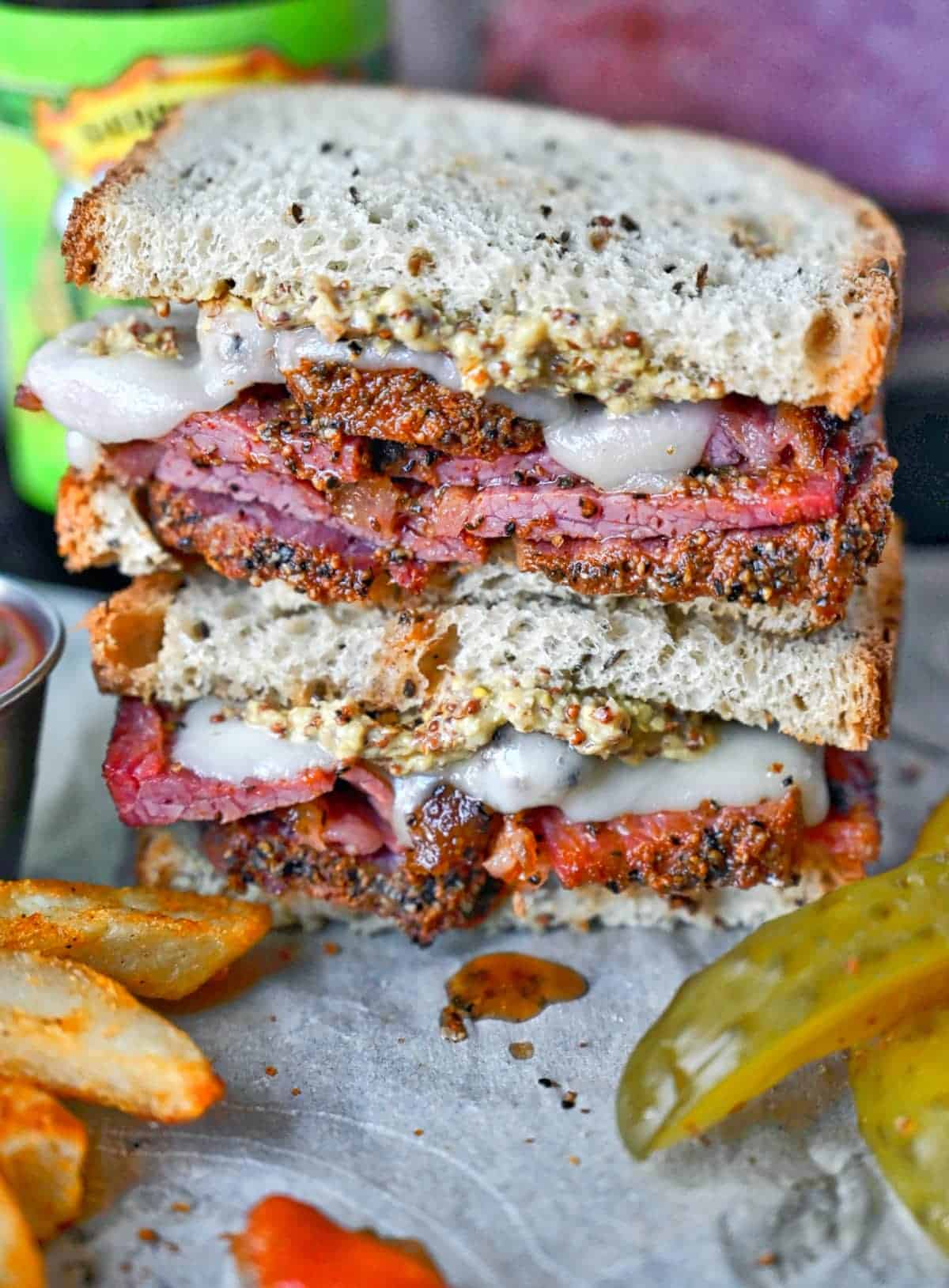 Slow cooker pastrami sandwich with seasoned fries and pickles.