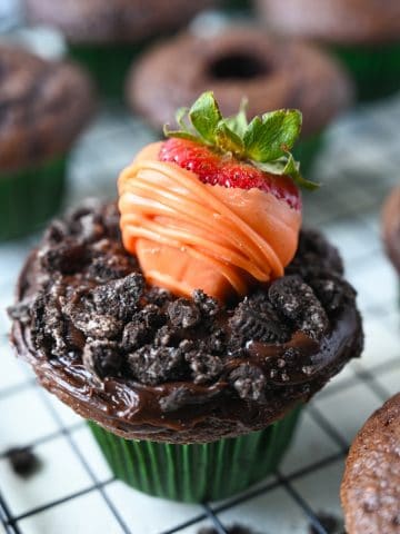 Chocolate dipped strawberry that looks like a carrot on top of a chocolate frosted cupcake with oreo crumbles on top to look like dirt.